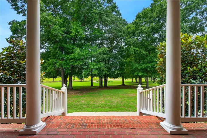 A classic brick porch extends to a verdant landscape framed by mature trees, offering a tranquil vista.