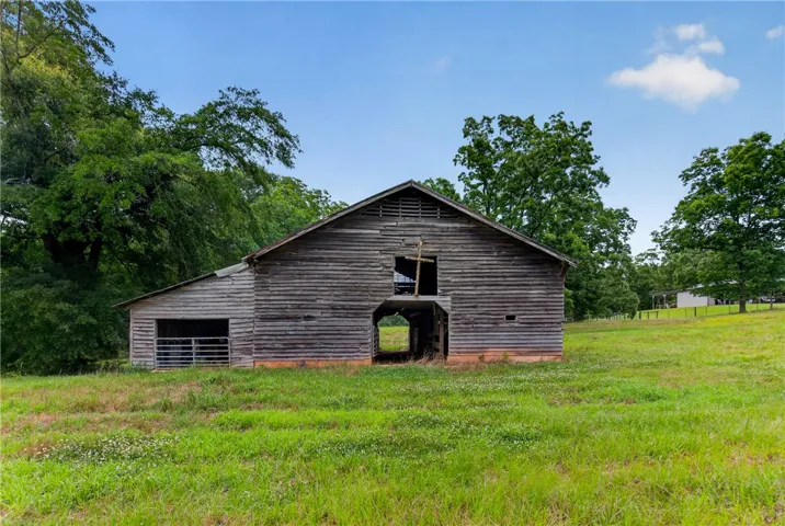 An aged wooden barn stands weathered against a verdant field, framed by mature trees.