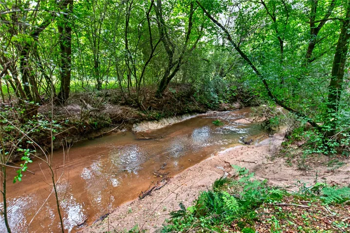 A tranquil stream meanders through a verdant, wooded landscape, offering a serene natural boundary.