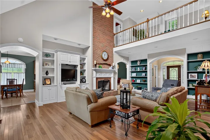 A spacious great room showcases soaring ceilings, a stately brick fireplace, and built-in shelving, with hardwood floors extending throughout.
