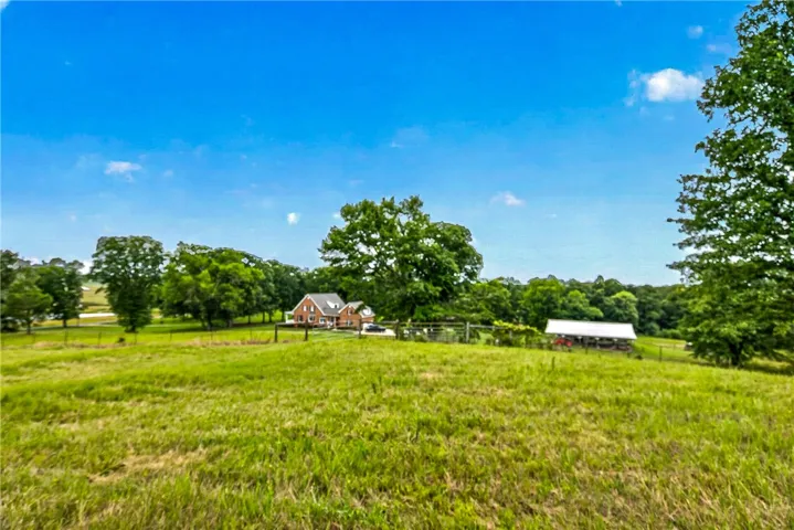 Green pastures with ample space for animals surround a brick home and detached shed.