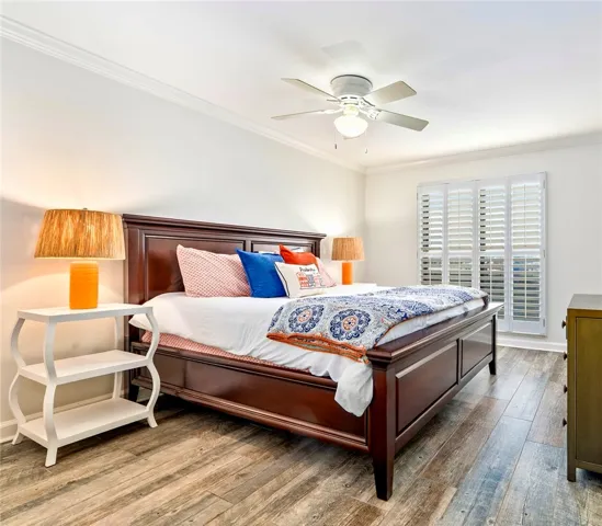 A well-lit bedroom features crown molding and wood-look flooring.