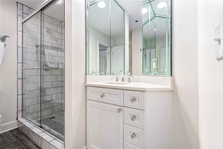 Marble-tiled shower alongside a contemporary white vanity with stylish drawer pulls.