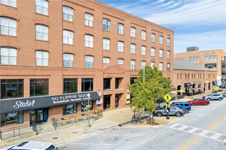 A vibrant downtown streetscape showcases a multi-story brick building with commercial storefronts and street parking.