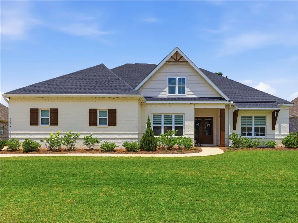 Well-maintained grounds frame this appealing home with a dark shingle roof and contrasting white brick.