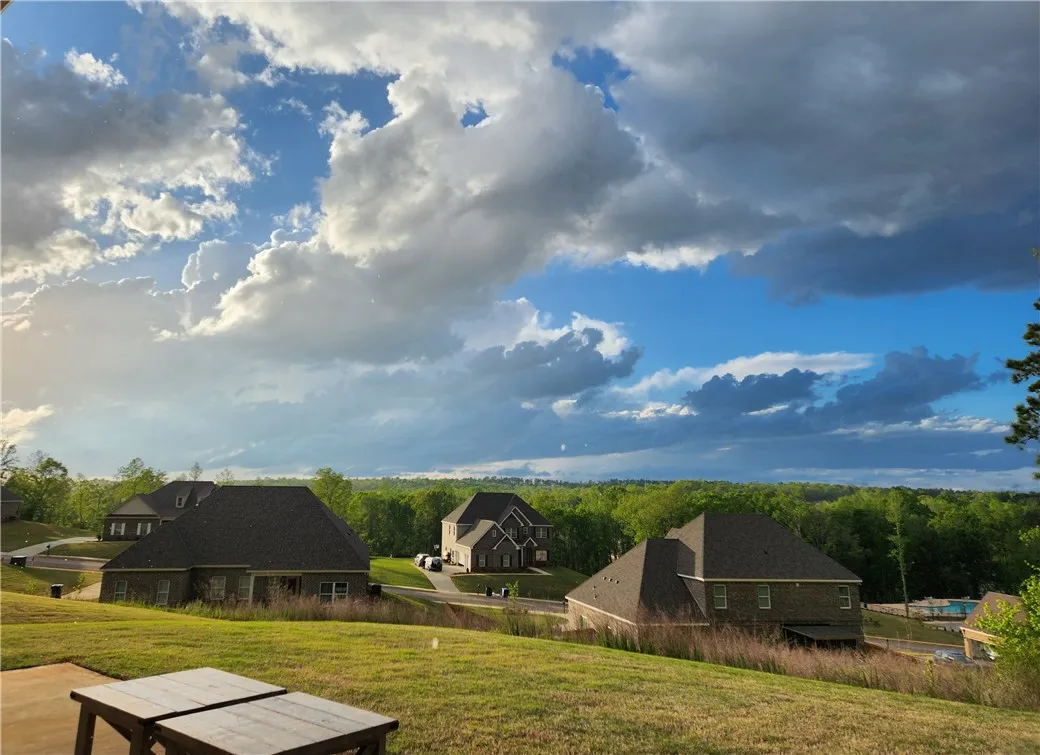 Rolling green landscape with distant homes under a dramatic, cloud-filled sky.