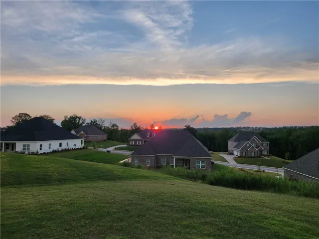 Golden hour illuminates a serene neighborhood with rolling green lawns and distant treelines.