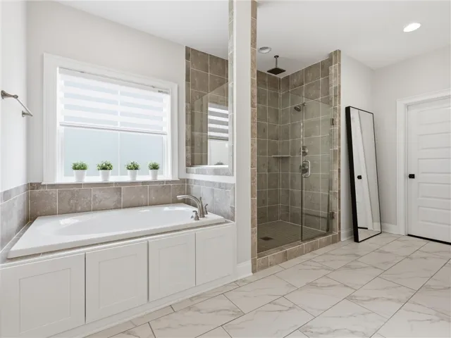 Indulge in a relaxing soak within this naturally illuminated bathroom, featuring a deep tub and a spacious, glass-enclosed shower.
