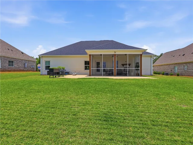 A pristine lawn stretches towards a home featuring a charming screened porch and spacious patio.