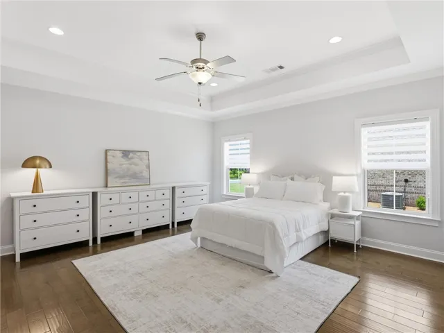 A tranquil primary bedroom with rich hardwood floors and elegant tray ceilings.
