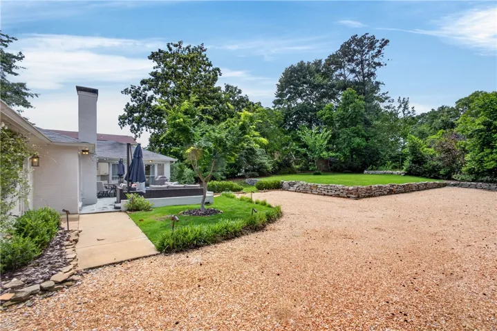 A spacious gravel driveway leads to a private patio surrounded by lush greenery and stone retaining walls.