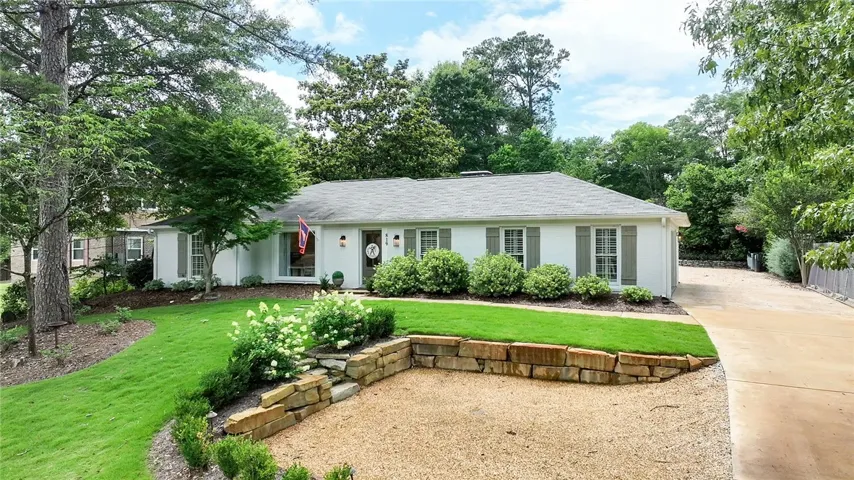 A classic ranch home nestled among mature trees features a well-kept lawn and a multi-surface driveway.