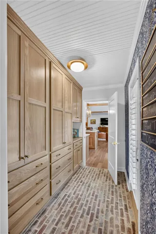 A well-organized hallway with custom wooden cabinetry and a unique brick flooring, leading to a sunlit interior.
