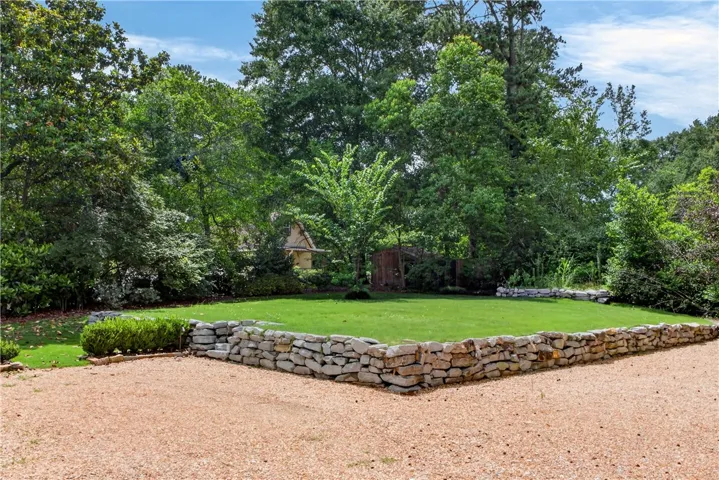 A well-maintained lawn with rustic stone retaining walls provides a private yard amidst a wooded backdrop.