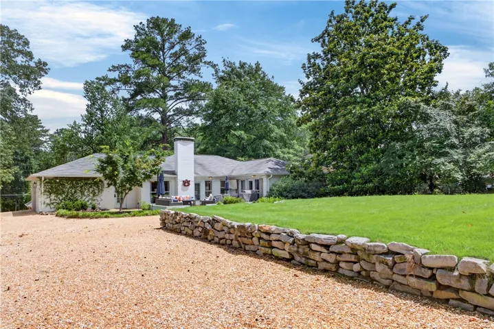 A graceful home sits back from a gravel driveway, accented by a charming stone wall and verdant trees.