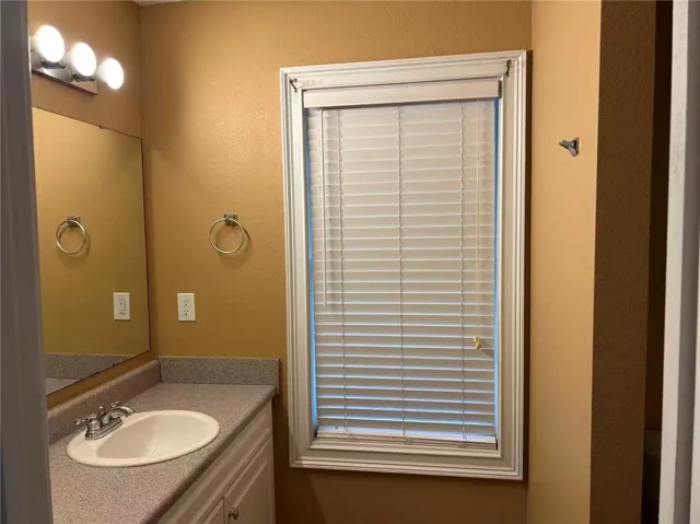 A window with blinds illuminates a well-appointed bathroom vanity.