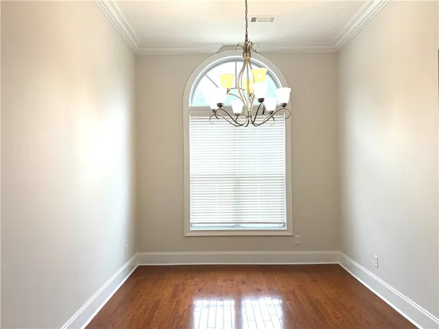 Hardwood flooring and crown molding define this versatile interior space, illuminated by an arched window.
