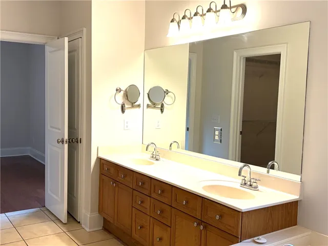 Double vanity with light wood cabinetry and a large mirror provides ample space for personal routines.