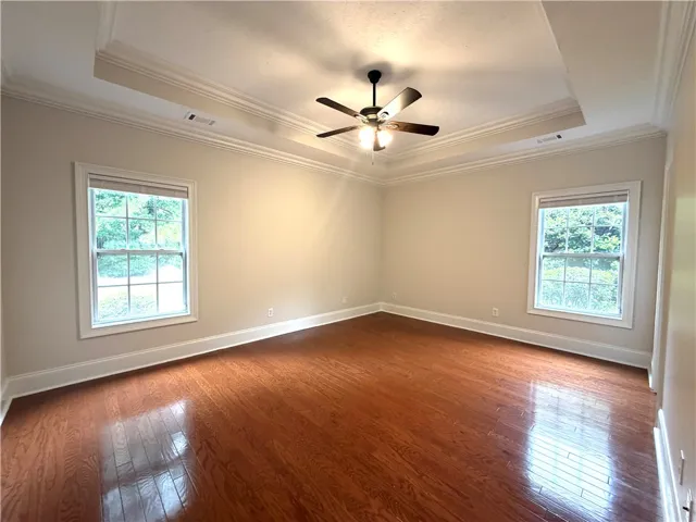 Rich hardwood floors complement tray ceilings in this naturally illuminated bedroom space.