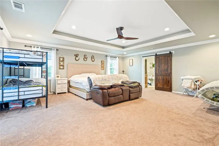 A spacious bedroom features a tray ceiling, recessed lighting, and a charming barn door leading to an adjoining area.