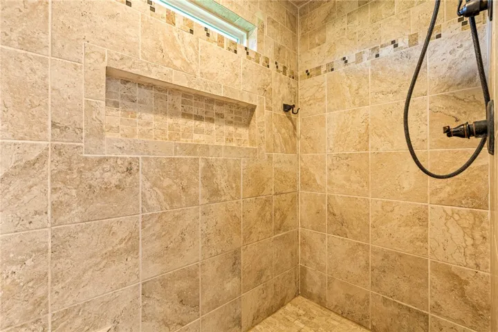 A well-appointed shower features natural stone tiling, an integrated niche, and a window for natural light.