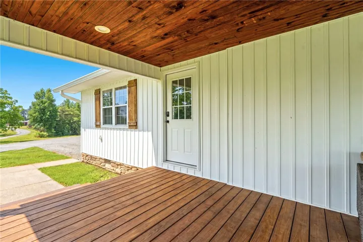 A welcoming front porch features rich wood decking, framed by crisp white siding and rustic window shutters.