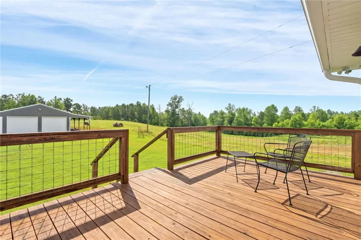 A spacious wooden deck provides tranquil views of a sprawling, verdant landscape and distant outbuilding.