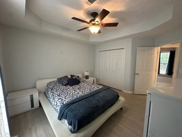 Recessed lighting and a ceiling fan adorn this primary bedroom with elegant flooring.