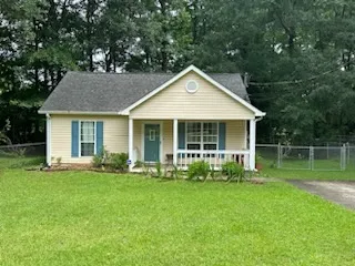 An inviting front porch welcomes you to this charming residence, framed by mature trees and a lush green lawn.
