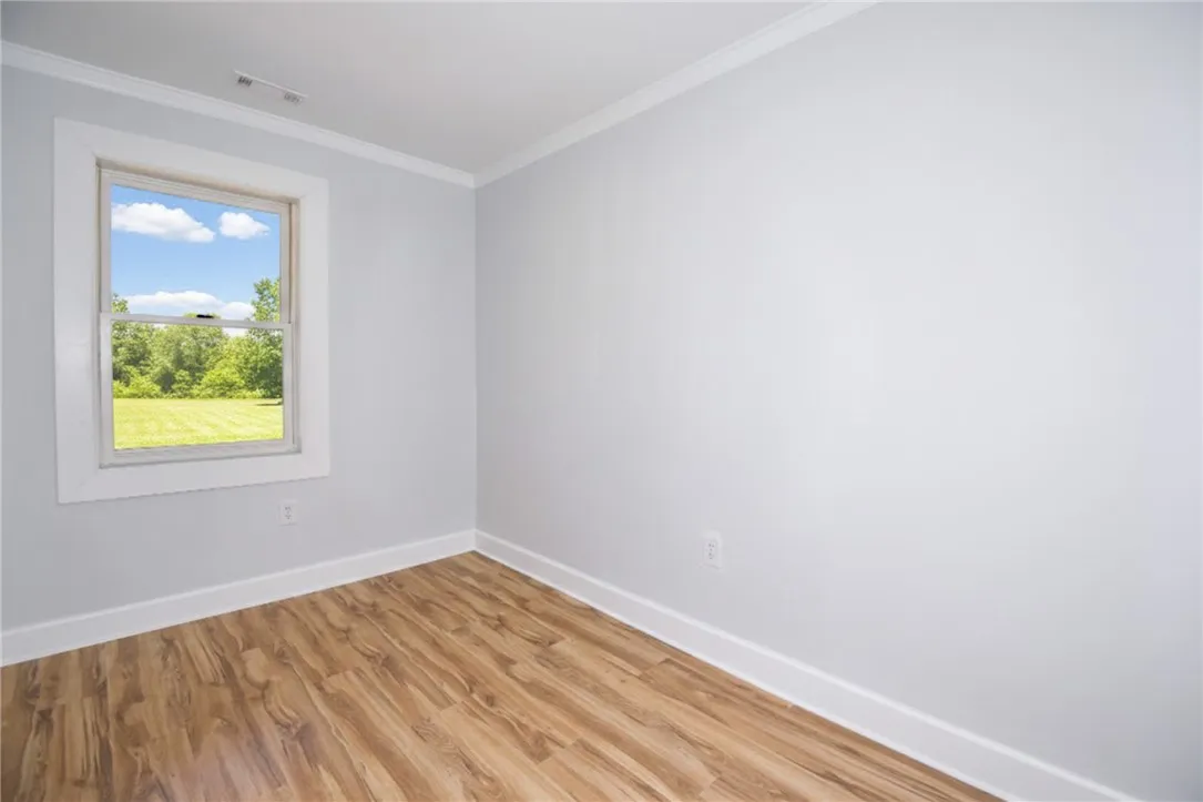 A well-lit room features durable laminate flooring and a serene view of green landscape through the window.
