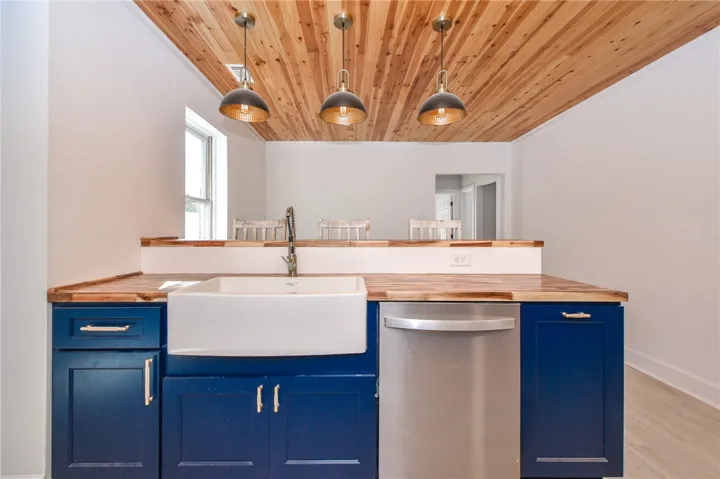 A stylish kitchen presents rich blue cabinetry and natural wood countertops, illuminated by three pendant lights.