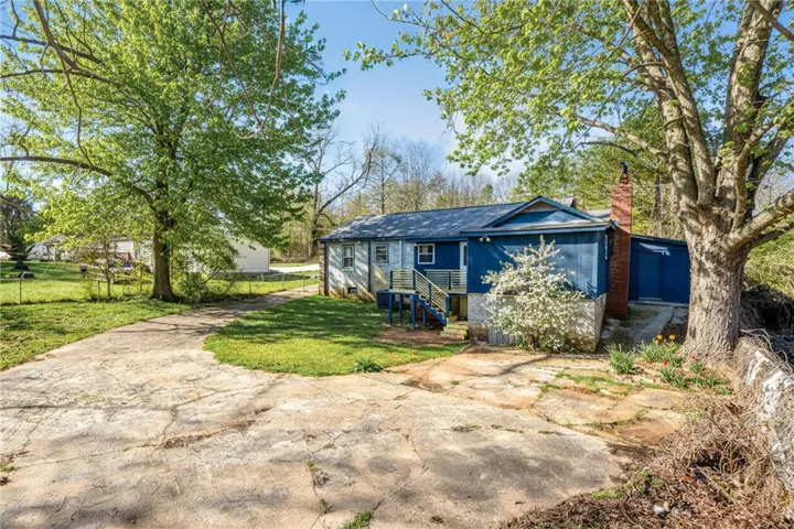 Mature trees frame this modest blue residence with a concrete drive and ample yard space.