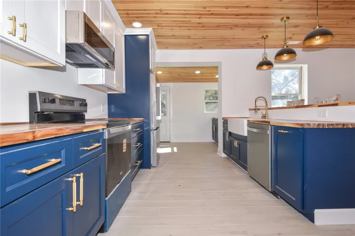 A vibrant kitchen boasts blue cabinetry, natural wood countertops, and modern appliances under a striking wood-paneled ceiling.