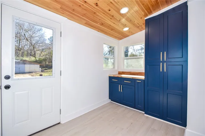 Bright laundry area featuring warm wood ceilings, deep blue cabinetry, and outdoor access.