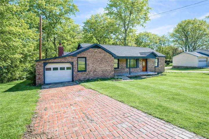Brick residence with attached garage and a complementary detached garage, nestled amidst mature trees.