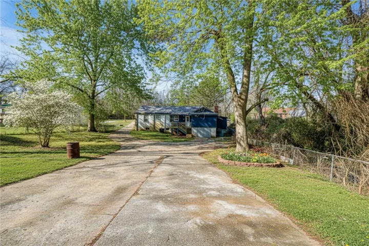 A private driveway leads to a modest home nestled among mature trees and vibrant spring blooms.