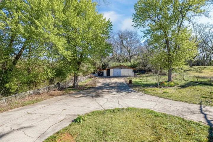 Mature trees frame a long concrete driveway leading to a secluded shed, nestled within a generous lot.