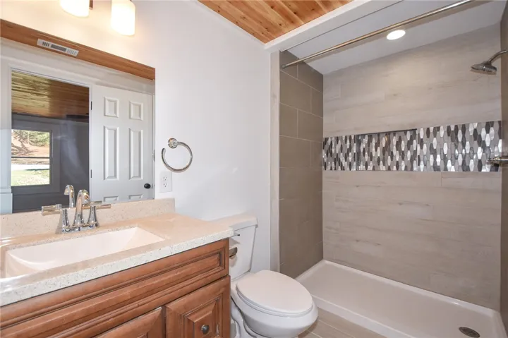 A well-appointed bathroom features a spacious shower with striking tile accents and a warm wood ceiling.