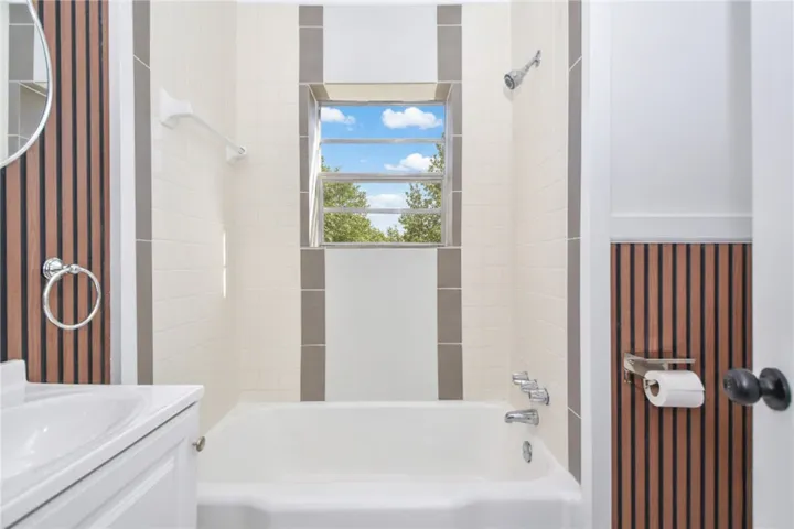 A well-lit bathroom features a deep soaking tub and a window overlooking green trees.