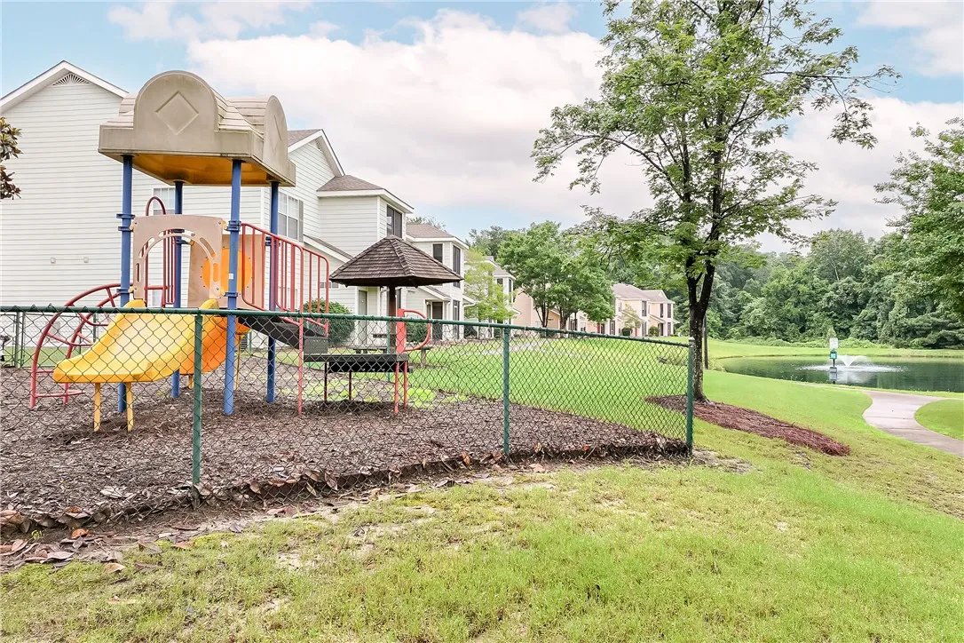 A well-maintained playground awaits  residents, adjacent to a pond and walking path.