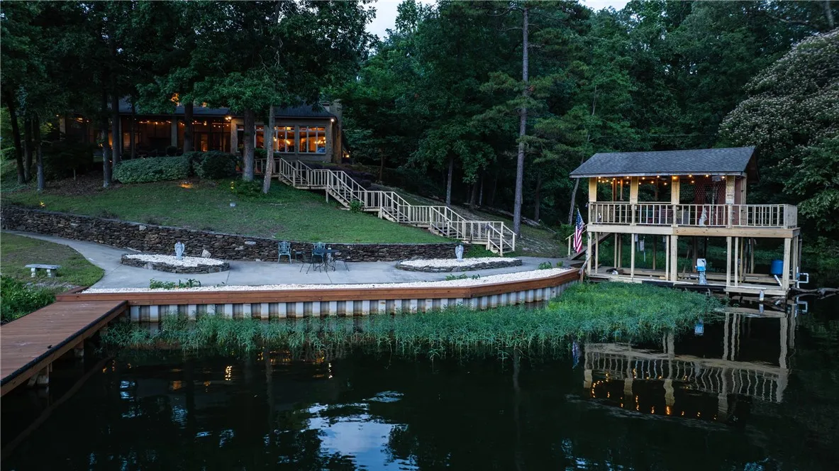A tranquil lakeside estate features extensive outdoor living space and a private boat dock with an upper-level deck.