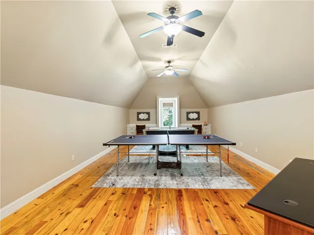 A vibrant game room with high vaulted ceilings and polished hardwood flooring provides ample space for recreation.