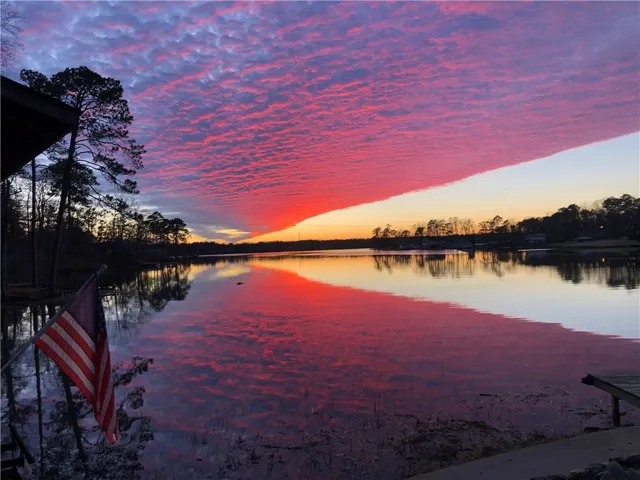Crimson and violet clouds adorn the sky above a serene lake reflecting the vibrant sunset.