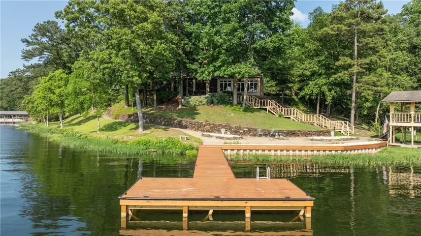 Lakeside home featuring a private dock and a charming boathouse nestled amongst mature trees.