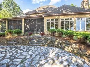 An inviting stone patio leads to a screened-in porch and large windows along the home's rear exterior.