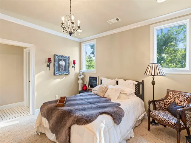 Step into this naturally illuminated bedroom featuring an elegant chandelier and plush carpeting.