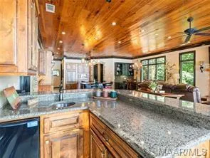 A well-lit open floorplan connects the kitchen's ample counter space to a welcoming living area, all beneath a rich wood-paneled ceiling.
