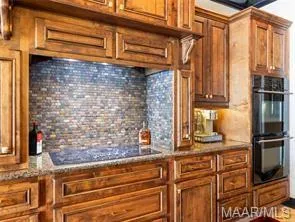 Rich wood cabinetry surrounds a sleek electric cooktop and modern double oven.