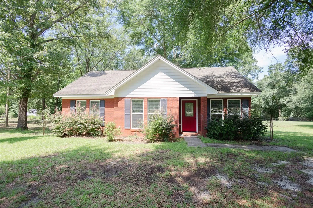 A charming brick Guest House with a vibrant red door, nestled amidst lush trees and green lawn.