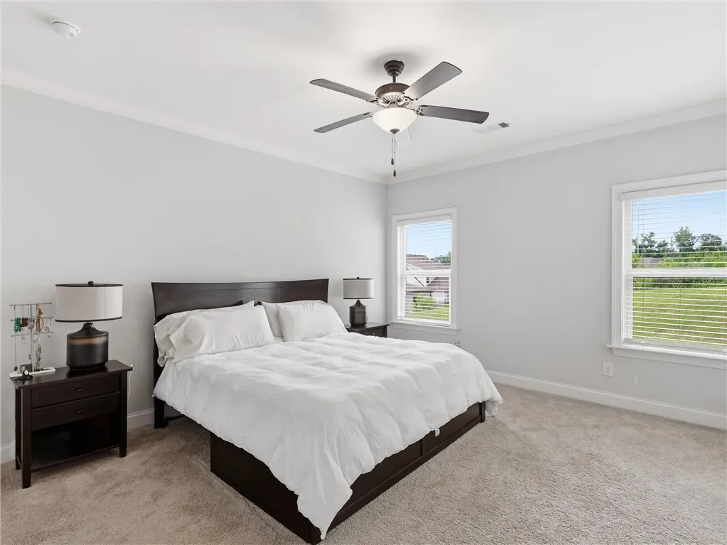 A tranquil primary bedroom with soft carpet, a dark wood bed, and large windows inviting natural light.